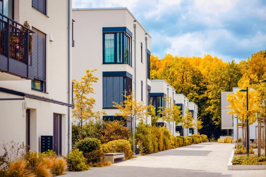 Modern white apartment buildings line a paved pathway surrounded by bright autumn trees.