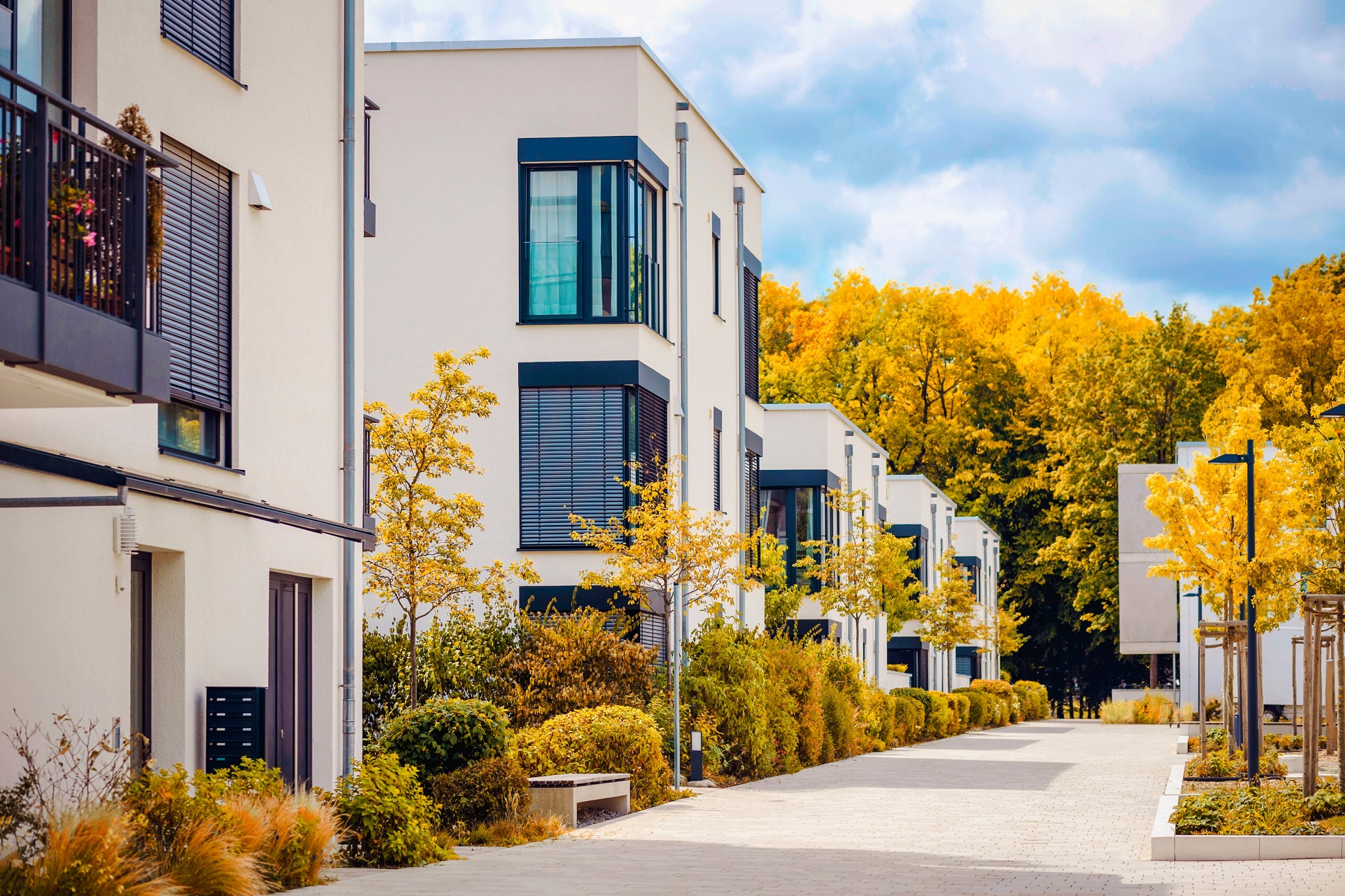 Modern white apartment buildings line a paved pathway surrounded by bright autumn trees.